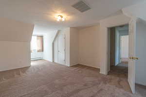 Additional living space featuring a textured ceiling, light carpet, and a baseboard heating unit