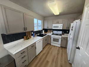Kitchen with white appliances, light wood-style flooring, a textured ceiling, and gray cabinets