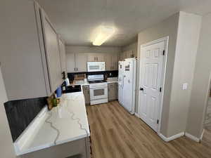 Kitchen featuring white appliances, light wood-type flooring, light stone countertops, a textured ceiling, and gray cabinets