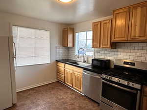 West Kitchen with appliances with stainless steel finishes, dark countertops, brown cabinets, and decorative backsplash