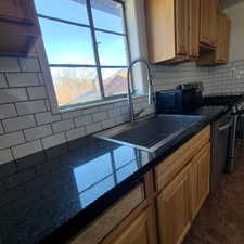 West unit Kitchen with appliances with stainless steel finishes, backsplash, brown cabinetry, and dark tile patterned floors