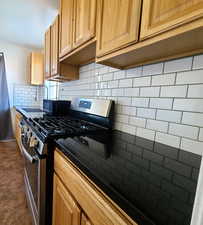 West unit Kitchen with stainless steel range with gas cooktop, black microwave, decorative backsplash, dark countertops, and light brown cabinets