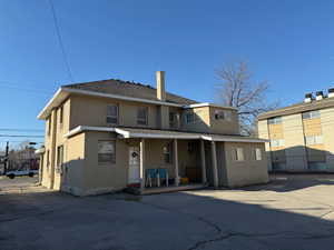 Rear view of house with stucco siding, a chimney, and roof with shingles