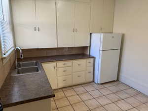 Kitchen featuring dark countertops, freestanding refrigerator, light tile patterned flooring, and tasteful backsplash