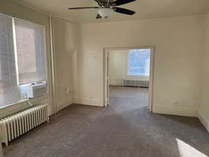 Carpeted spare room with radiator heating unit, cooling unit, and a ceiling fan