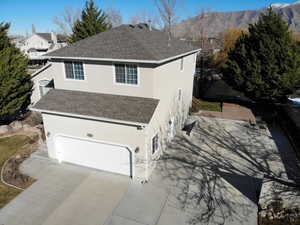 View of side of property with a shingled roof, stucco siding, an attached garage, and concrete driveway
