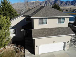 View of front facade with roof with shingles, stucco siding, a garage, and driveway