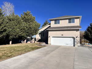 Traditional-style house with stucco siding, a garage, driveway, a front yard, and roof with shingles
