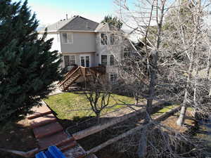 Back of house featuring stairs, roof with shingles, a wooden deck, a yard, and stucco siding