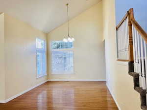 Unfurnished dining area featuring high vaulted ceiling, wood finished floors, and a chandelier