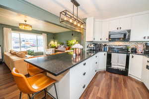Kitchen featuring black appliances, open floor plan, a peninsula, white cabinets, and dark wood-style flooring