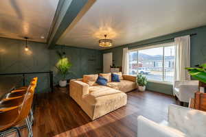 Living area featuring a decorative wall, dark wood-style floors, a chandelier, an accent wall, and beam ceiling