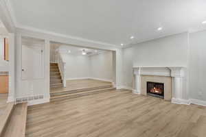 Unfurnished living room with light wood finished floors, a tile fireplace, ceiling fan, stairway, and recessed lighting