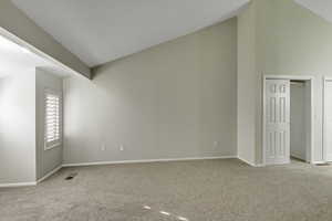 Primary bedroom with high vaulted ceiling and light colored carpet
