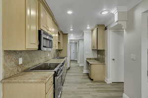 Kitchen with light brown cabinetry, stainless steel appliances, backsplash, light stone counters, and light wood-type flooring