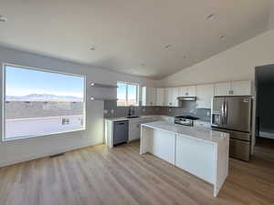 Kitchen with light stone countertops, stainless steel appliances, decorative backsplash, white cabinetry, and high vaulted ceiling
