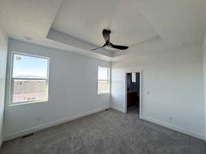 Unfurnished bedroom with a raised ceiling, carpet floors, ceiling fan, and ensuite bathroom