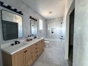Bathroom featuring double vanity, light marble finish floors, and tile walls