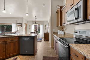 Kitchen featuring appliances with stainless steel finishes, hanging light fixtures, brown cabinets, light stone counters, and a textured ceiling