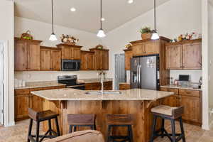 Kitchen featuring brown cabinets, a kitchen bar, stainless steel appliances, pendant lighting, and vaulted ceiling