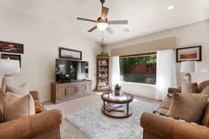 Living area featuring a ceiling fan, carpet flooring, and lofted ceiling