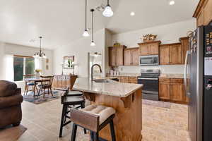 Kitchen featuring brown cabinets, stainless steel appliances, light stone counters, pendant lighting, and a kitchen breakfast bar