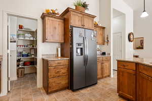 Kitchen featuring stainless steel fridge, light stone countertops, decorative light fixtures, and brown cabinetry