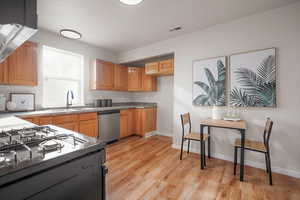 Kitchen featuring gas range, stainless steel dishwasher, extractor fan, light wood-style floors, and brown cabinetry