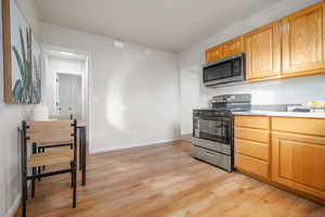 Kitchen with appliances with stainless steel finishes, light wood-style flooring, light stone countertops, and light brown cabinets