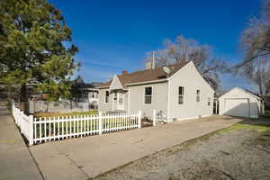 View of front of house with concrete driveway, a chimney, an outdoor structure, a fenced front yard, and a detached garage