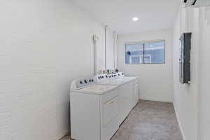 Washroom with separate washer and dryer, electric panel, and brick wall