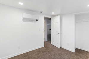 Unfurnished bedroom featuring a wall unit AC and dark carpet