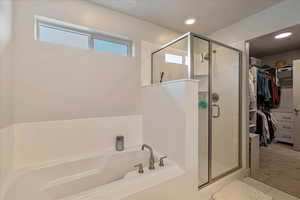 Full bathroom with a walk in closet, a stall shower, a bath, light tile patterned floors, and light colored carpet