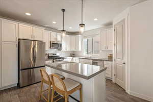 Kitchen featuring stainless steel appliances, a breakfast bar area, white cabinets, a kitchen island, and decorative light fixtures