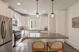 Kitchen with appliances with stainless steel finishes, white cabinets, decorative light fixtures, dark wood-style floors, and a kitchen breakfast bar
