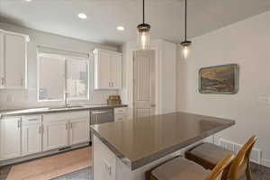 Kitchen featuring white cabinets, dark countertops, backsplash, a kitchen bar, and recessed lighting