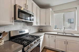 Kitchen with appliances with stainless steel finishes, white cabinetry, tasteful backsplash, and dark stone countertops