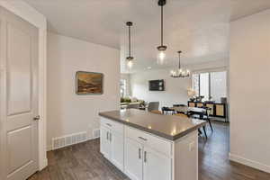 Kitchen with white cabinetry, hanging light fixtures, dark countertops, a kitchen island, and dark wood finished floors