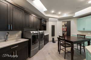 Laundry room featuring washer and clothes dryer, a tray ceiling, cabinet space, recessed lighting, and light flooring