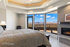 Bedroom featuring a mountain view, access to exterior, recessed lighting, a glass covered fireplace, and a tray ceiling