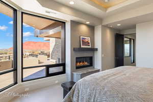 Bedroom featuring access to outside, a glass covered fireplace, tile patterned floors, recessed lighting, and a raised ceiling