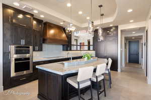 Kitchen with glass insert cabinets, light stone counters, a tray ceiling, tasteful backsplash, and recessed lighting