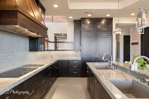 Kitchen with premium range hood, backsplash, light stone counters, recessed lighting, and black electric stovetop