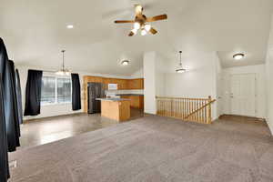 Kitchen featuring open floor plan, light carpet, white appliances, hanging light fixtures, and a kitchen island