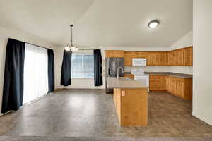 Kitchen with white appliances, a chandelier, lofted ceiling, a center island with sink, and hanging light fixtures