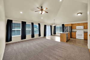 Kitchen with open floor plan, stainless steel appliances, a center island with sink, vaulted ceiling, and light colored carpet