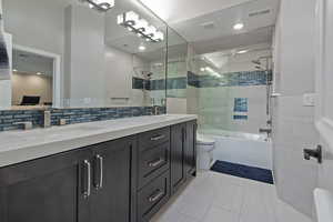 Bathroom featuring combined bath / shower with glass door, double vanity, light tile patterned floors, tasteful backsplash, and recessed lighting