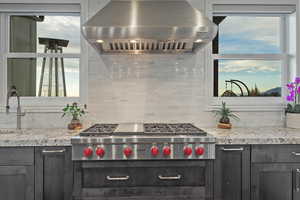 Kitchen with range hood, stainless steel gas stovetop, light stone countertops, and tasteful backsplash