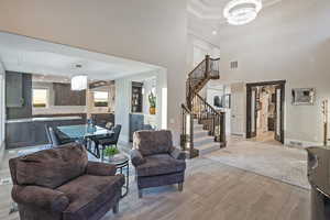 Living room featuring a chandelier, stairs, wood finish floors, a raised ceiling, and crown molding