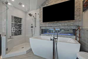 Bathroom with a soaking tub, a stall shower, recessed lighting, wood finished floors, and a multi sided fireplace
